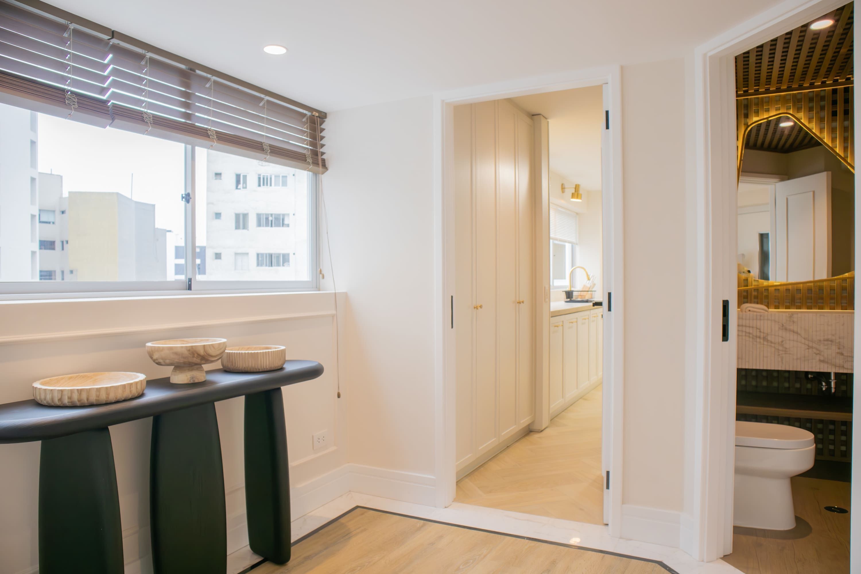Un bagno moderno con il water, un lavandino e uno specchio. Una finestra con persiane offre vista sugli edifici circostanti.
