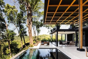 A modern outdoor pool area with a wooden pergola, surrounded by lush greenery and trees. - w Spectacular 4BR Villa in Costa Rica (Jacó)