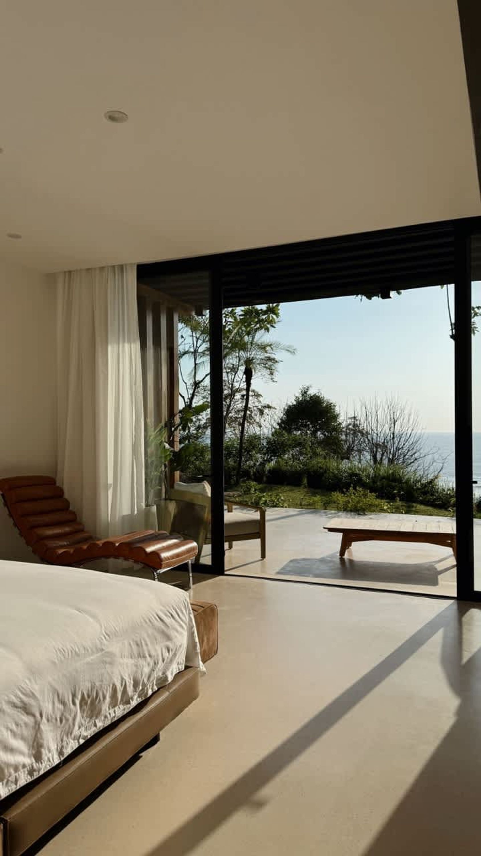 Un dormitorio moderno con una cama grande, una zona de estar con una silla y una mesa, y vistas al exterior.