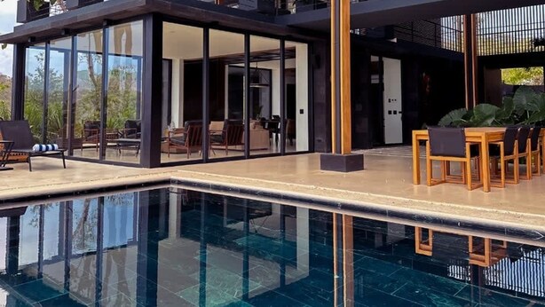 A modern pool area with a glass-enclosed lounge, wooden deck, and a view of the surrounding landscape. - w Spectacular 4BR Villa in Costa Rica (Jacó)