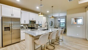Una cocina moderna con electrodomésticos de acero inoxidable, encimera de mármol y una isla central con taburetes de bar.