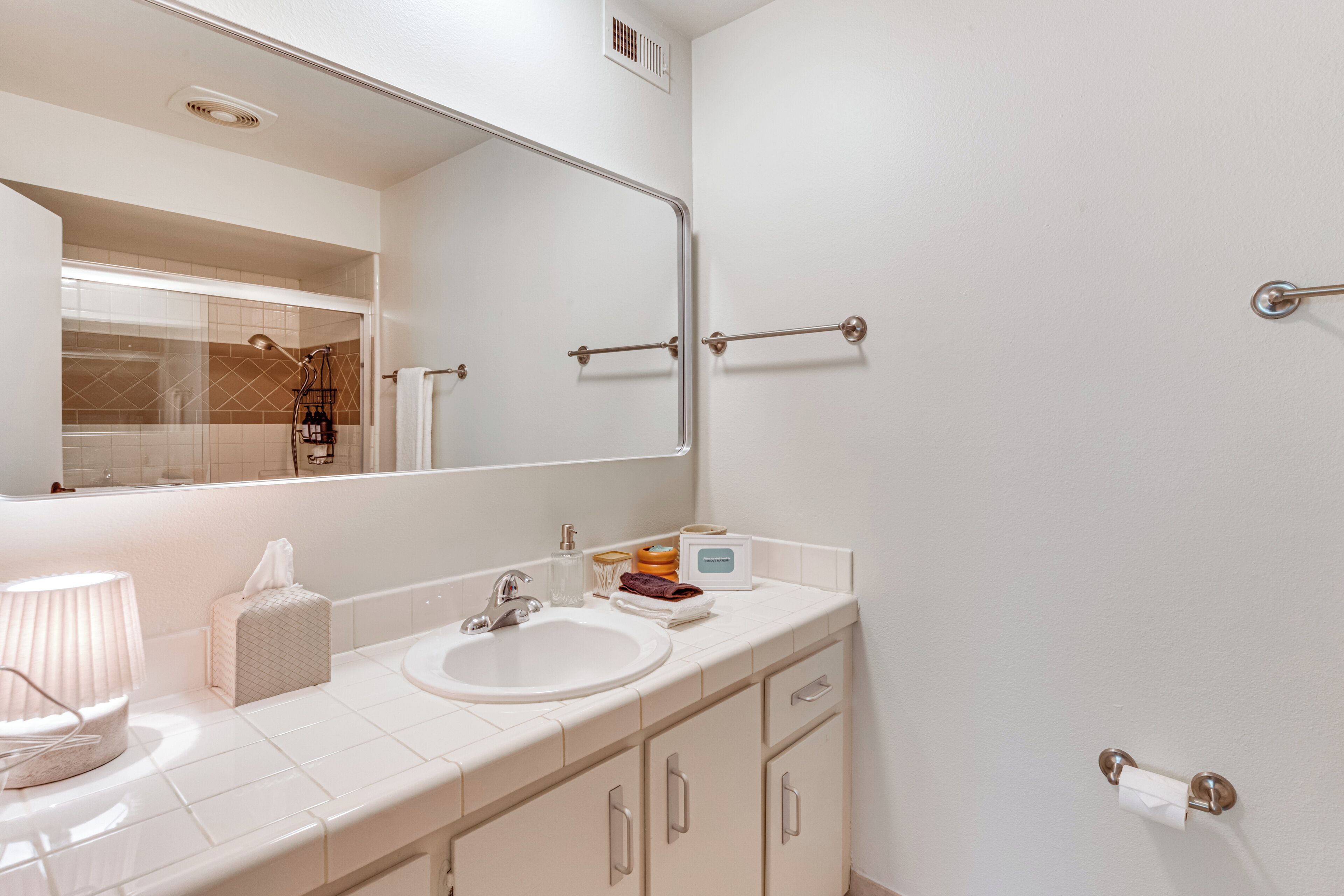 Une salle de bain moderne avec un grand miroir, des carreaux blancs, un lavabo et un porte-rouleau de papier toilette.