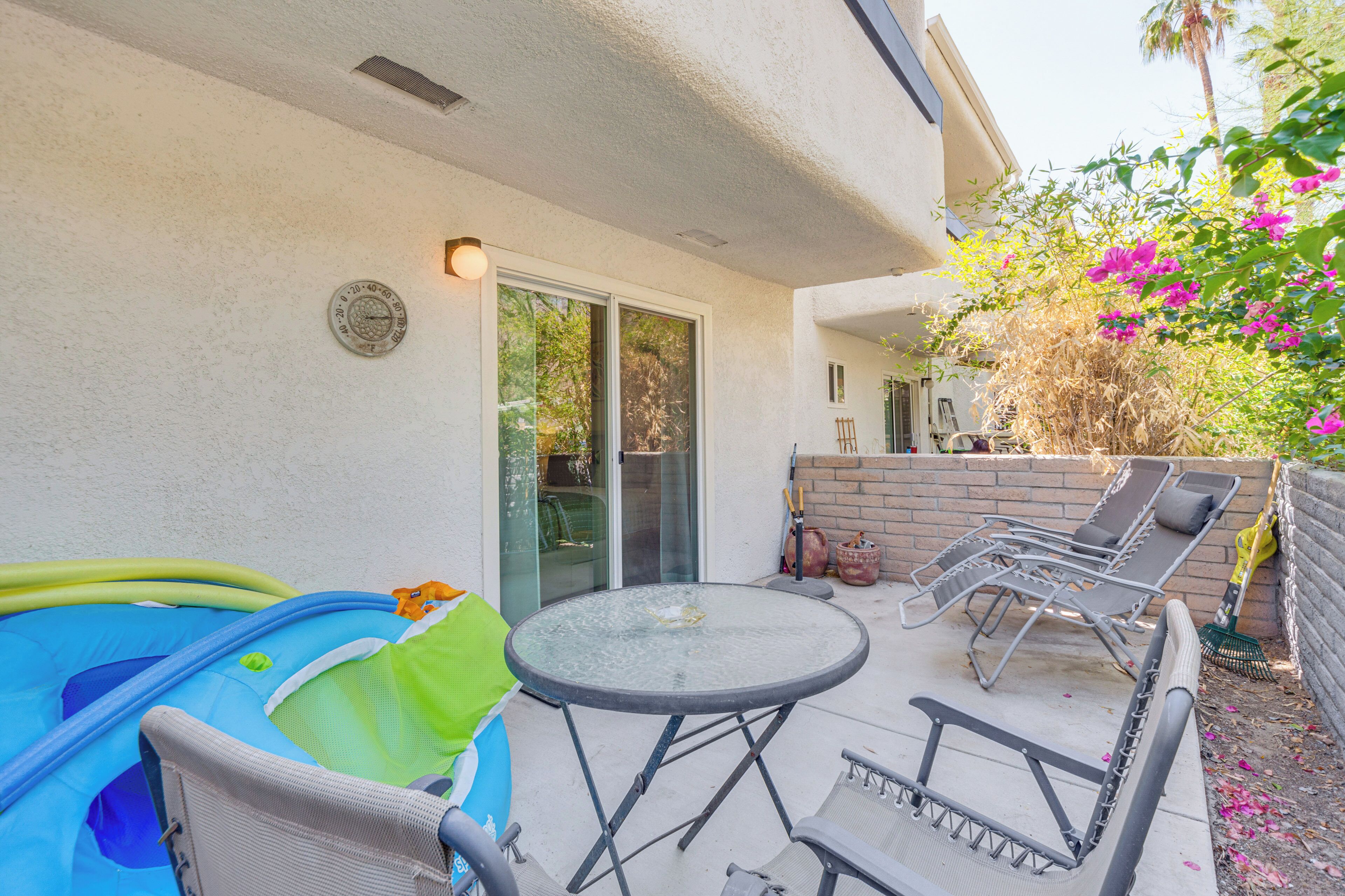 An outdoor patio with a round glass table, lounge chairs, and a small inflatable pool.