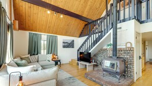 Un salón amplio con techo alto, chimenea, escalera y un área de descanso cómoda.