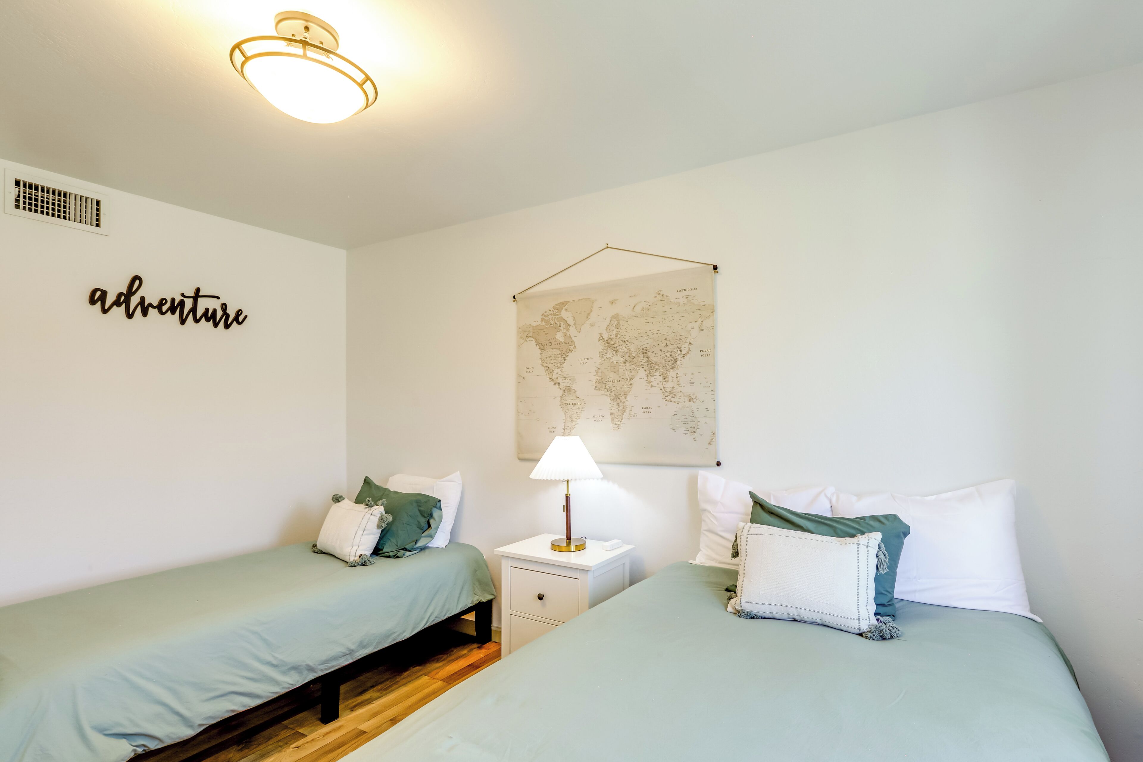 Una habitación con dos camas, un mapa mundial en la pared y un cartel que dice 'adventure'.