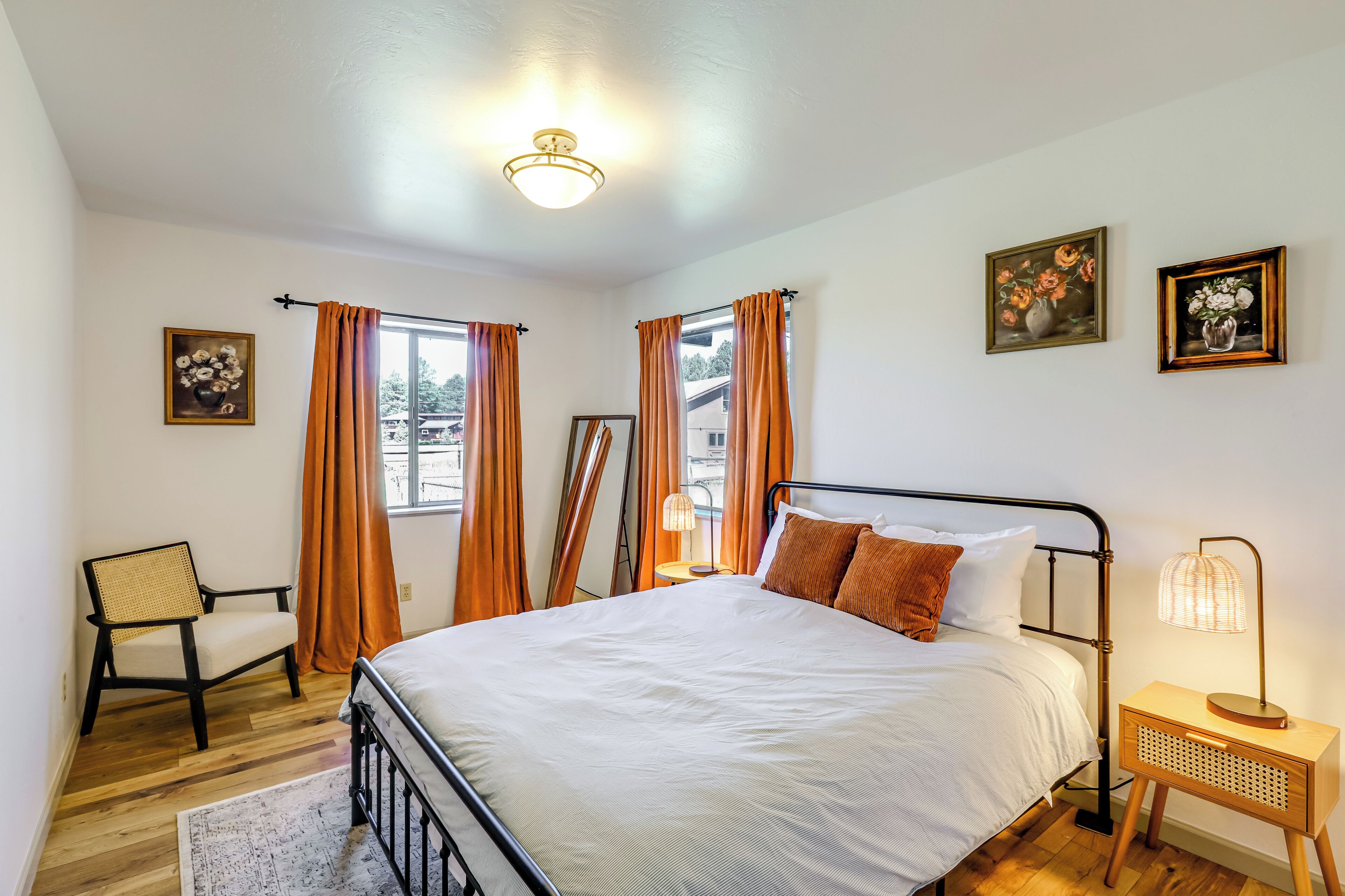 A bedroom with a bed, a chair, a nightstand, and two windows with curtains.