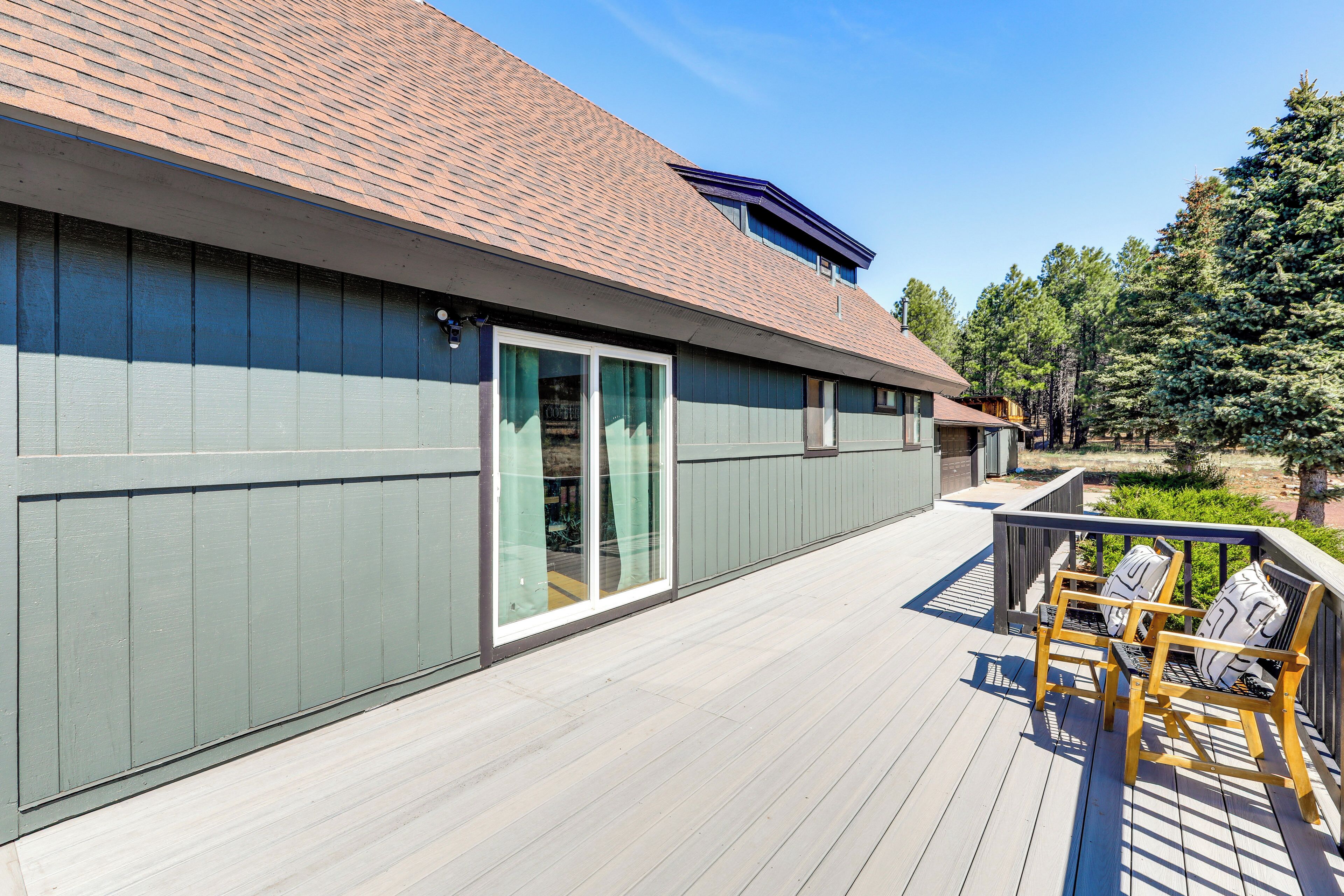 Un bâtiment moderne doté d’un toit plat, de grandes portes-fenêtres coulissantes et d’une terrasse en bois avec des espaces pour s’asseoir à l’extérieur.