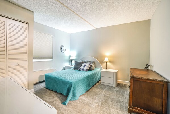 A bedroom with a bed, bedside tables, a clock, and a window with blinds.