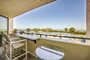 A balcony with a table and chairs, overlooking a pool and palm trees. - Pool Access & Waterfront Balcony: Hudson Condo! (Hudson)