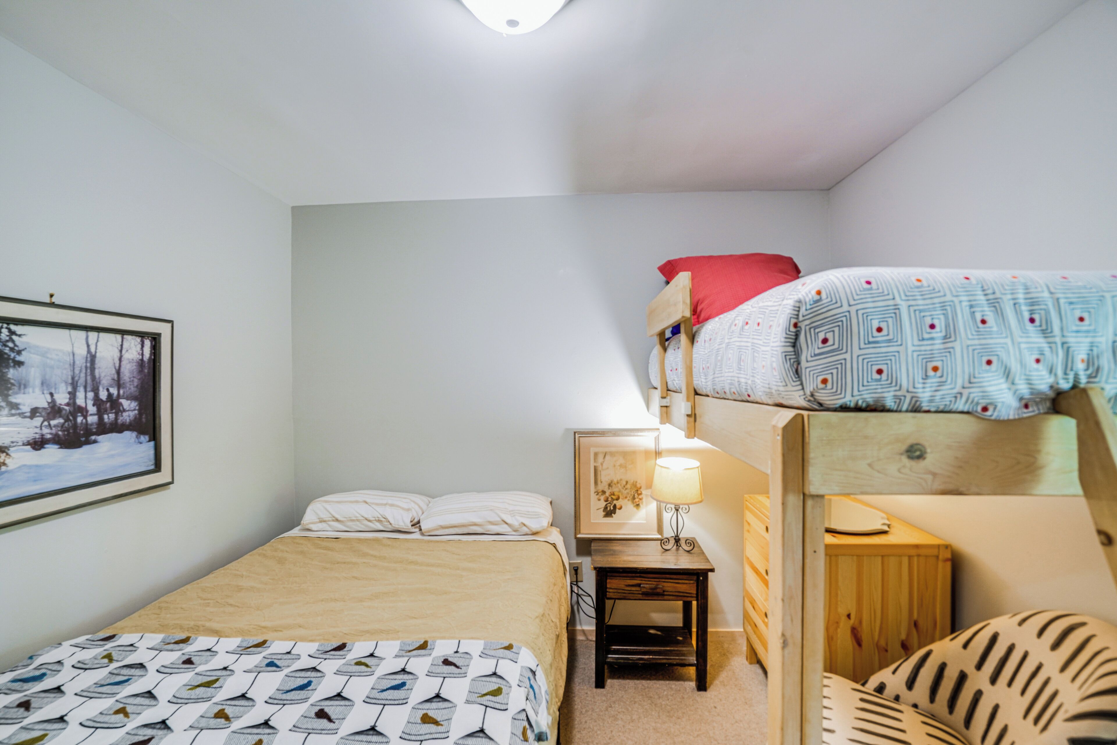 A dormitory room with bunk beds, a bedside table with a lamp, and a framed picture on the wall.