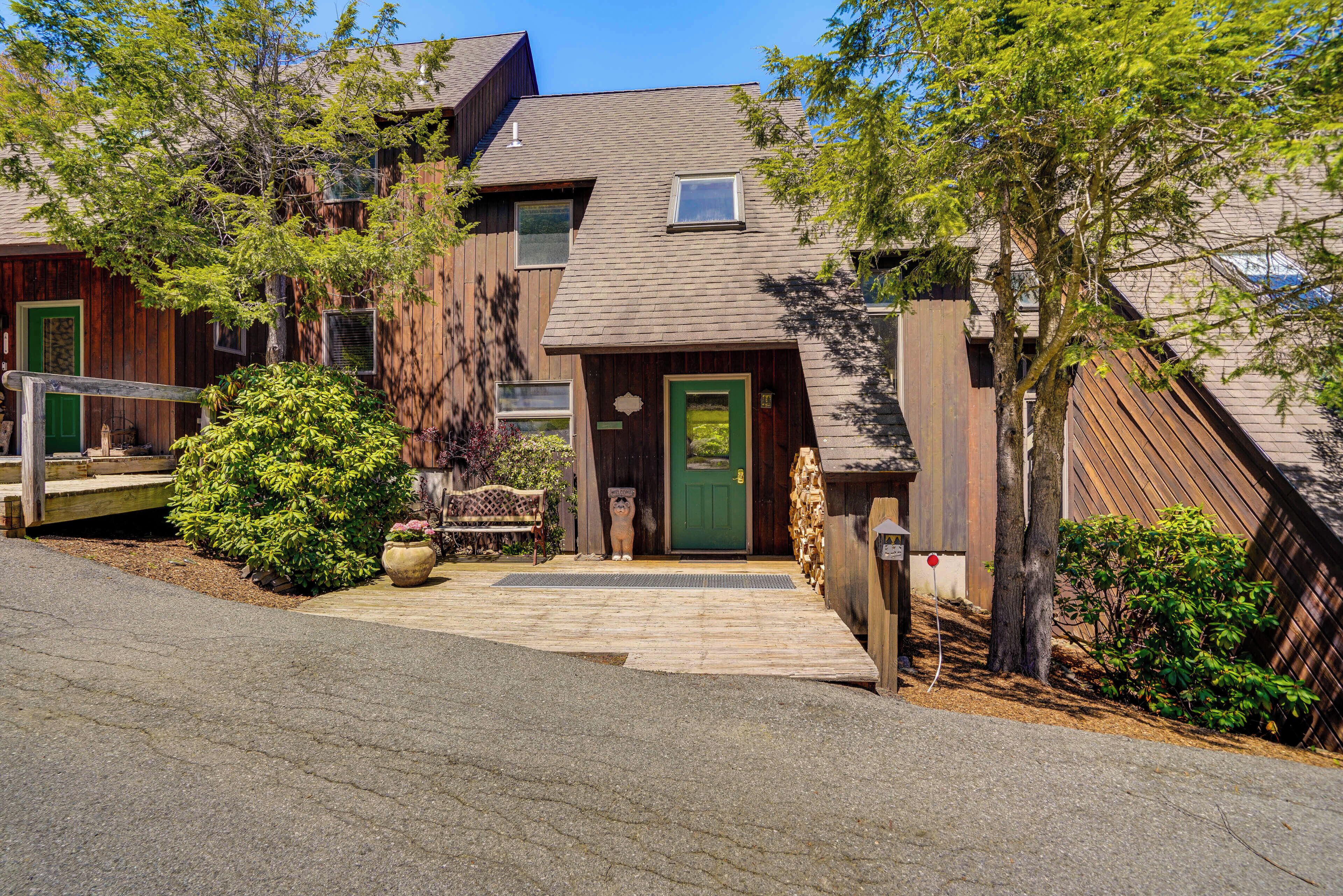 A two-story building with a green door, a wooden deck, and a small garden area with potted plants and a bench.