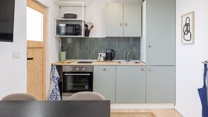 A compact kitchen with a microwave, oven, and sink. There is a wooden door and a small window. - Holiday Home Olive&sun (Zupa dubrovacka)