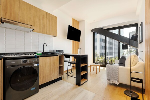 Eine moderne Küche mit integriertem Waschmaschine, einem Essbereich mit kleinem Tisch und Stühlen sowie einem großen Fenster mit Blick auf die Stadt.