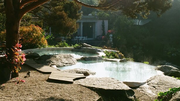 A hot spring surrounded by rocks and a wooden deck, with a gazebo and chairs in the background. - Tranquil 1BR Villa in Revislate (Veruno)