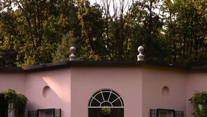 A building with a pink facade, a central arched window, and a pond with lily pads in front. - Tranquil 1BR Villa in Revislate (Veruno)