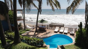 Zona de piscina con vista al océano, rodeada de palmeras y una terraza de madera.
