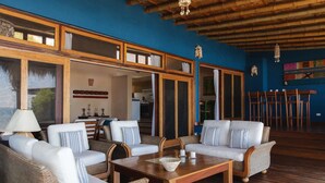 Amplia zona de estar al aire libre con muebles de mimbre y una mesa de madera, con vistas a un comedor con bar.
