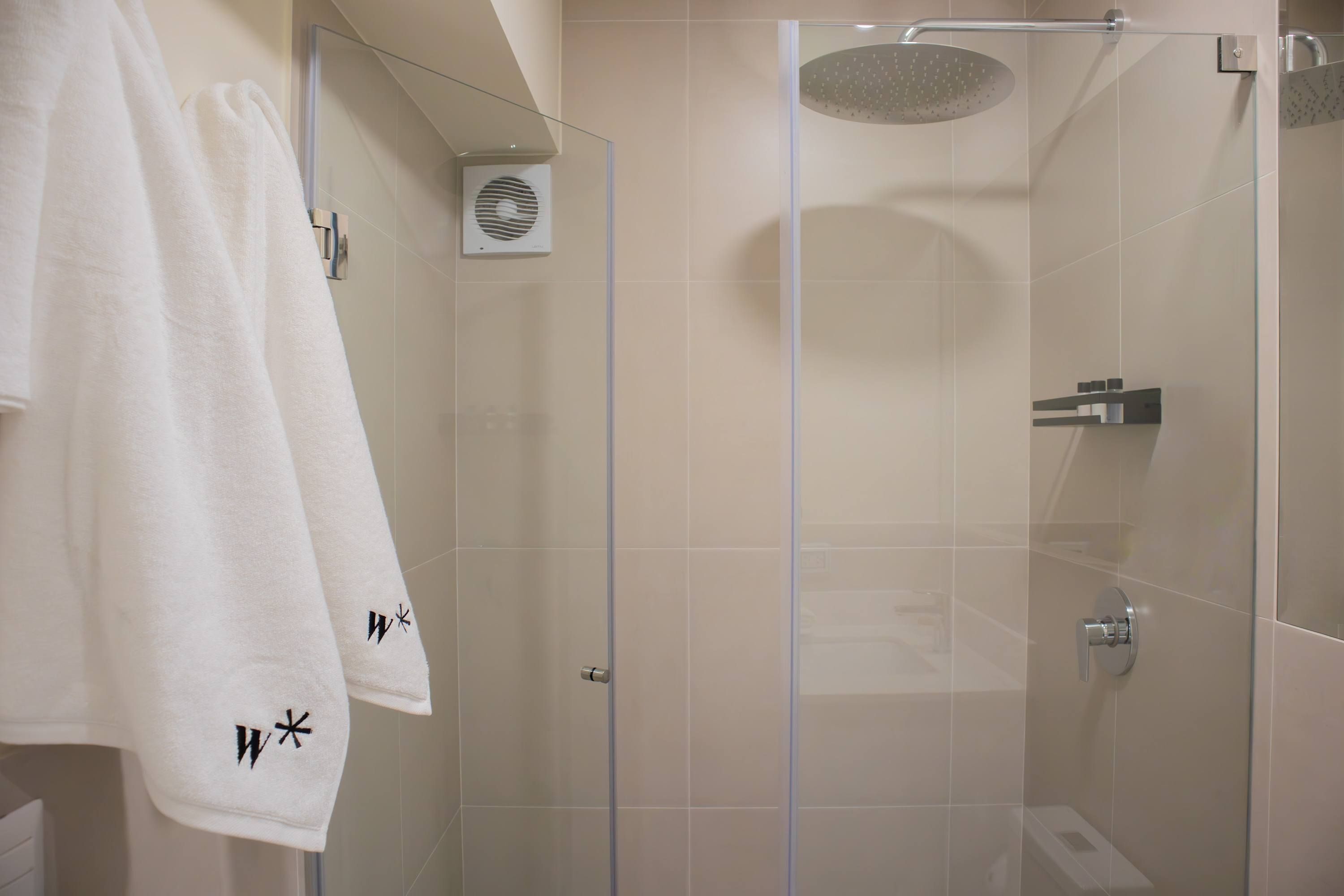 A modern bathroom with a glass-enclosed shower, white tiles, and towels hanging on a rack.