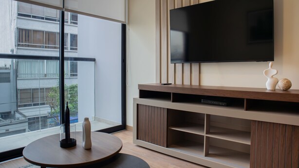 Un salon moderne avec un grand téléviseur fixé au mur, un meuble de rangement en bois en dessous, et une table basse ronde agrémentée de deux objets décoratifs.