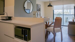 Une cuisine moderne dotée d’un four à micro-ondes encastré, d’un miroir rond et d’un coin repas avec une chaise en bois.