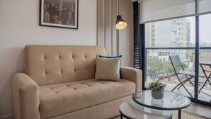 Un salon moderne avec un canapé beige, une table basse en verre et une vue sur la ville à travers de grandes fenêtres.