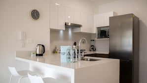 Une cuisine moderne avec des meubles blancs, un réfrigérateur en acier inoxydable, un four à micro-ondes encastré et une horloge murale.