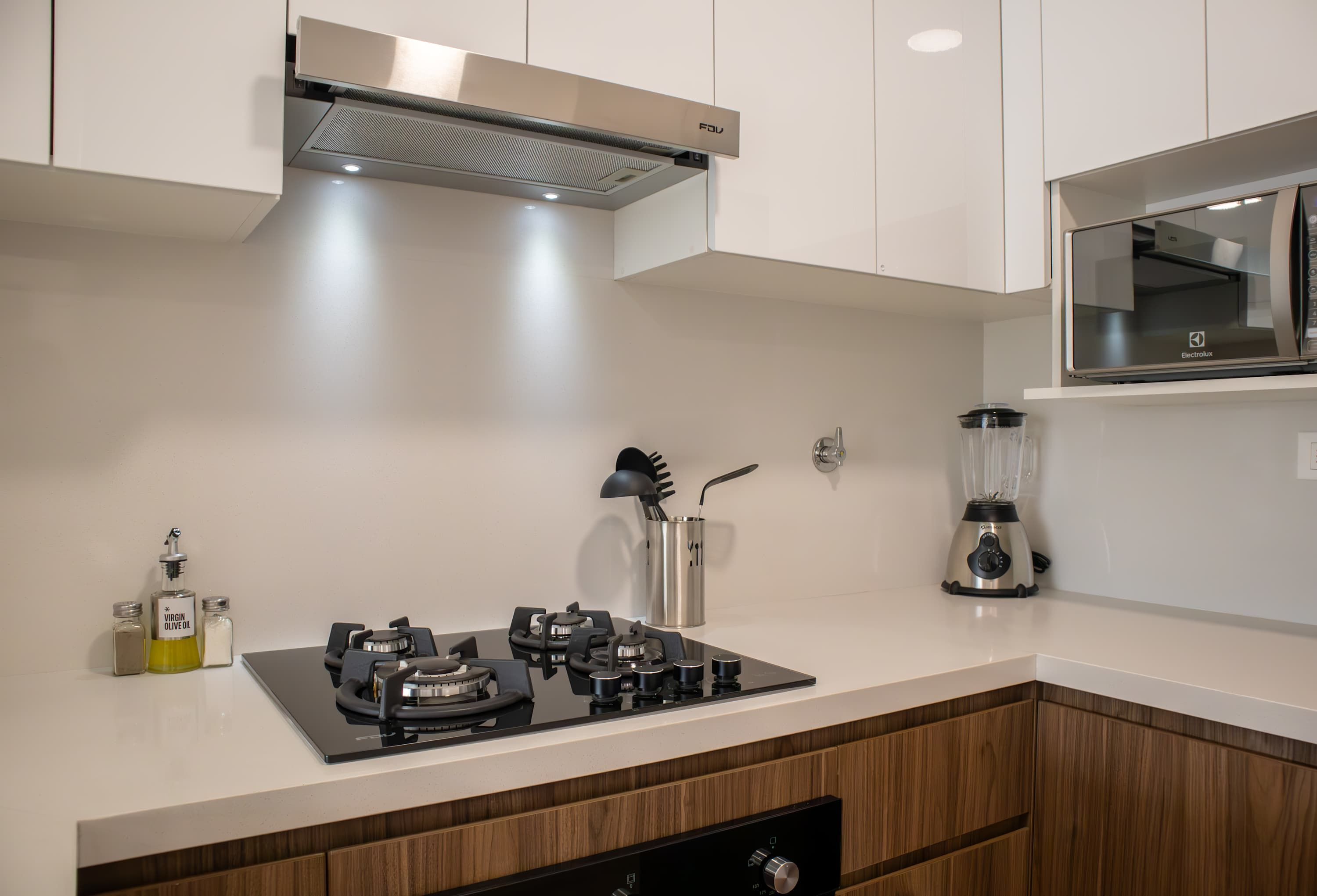 A modern kitchen with a gas stove, a blender, and a wooden cabinet.