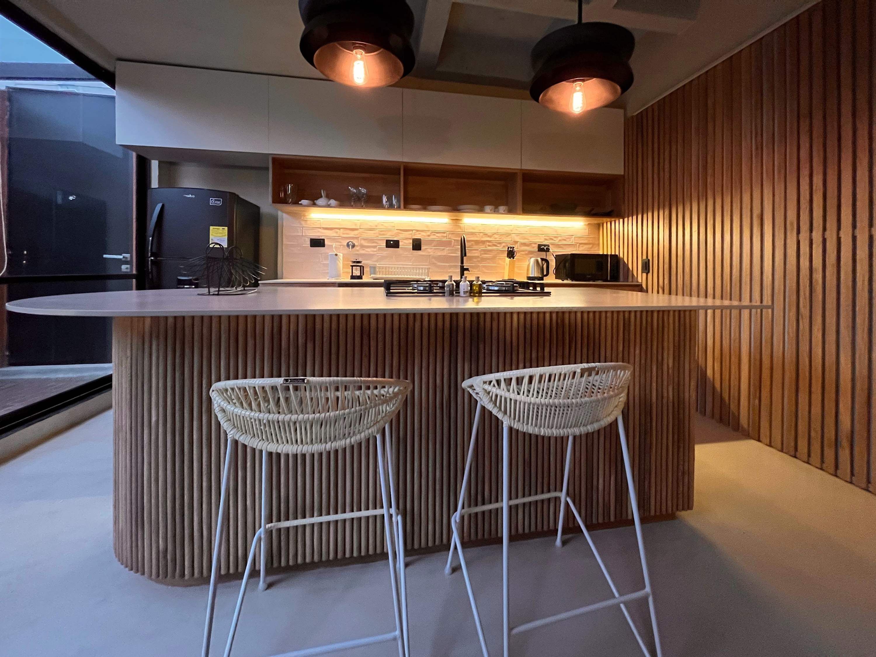 A modern kitchen with a central island, bar stools, and a refrigerator.