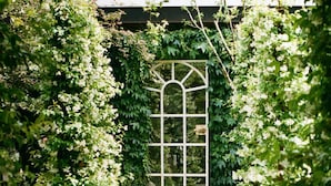 A garden pathway leading to a white arched window with a stone ball in the center. - Charming 1BR Suite in Revislate (Veruno)