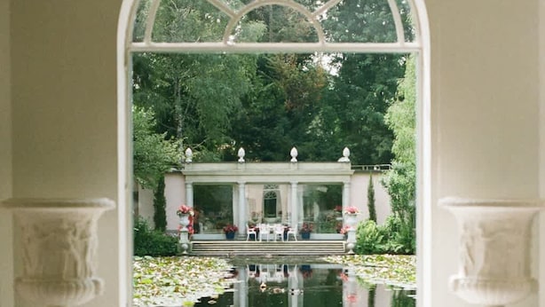 A view through a large arched window of a garden with a fountain, chairs, and a gazebo. - Charming 1BR Suite in Revislate (Veruno)