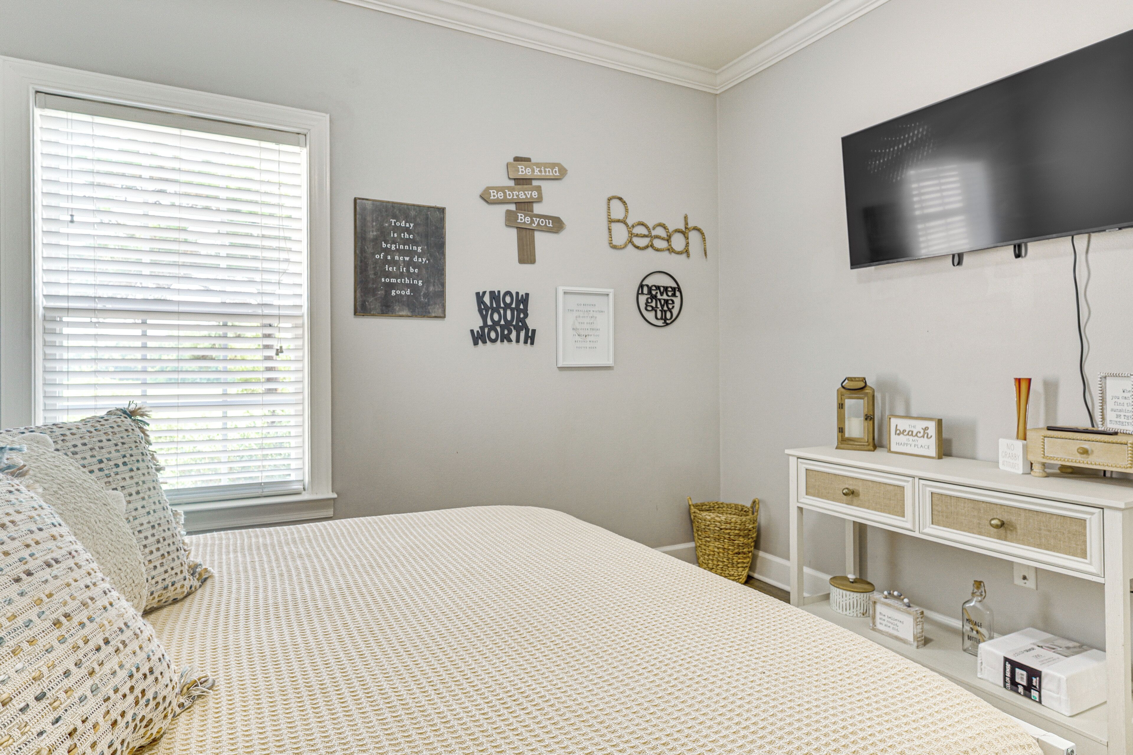 A bedroom with a bed, a television, a wall with motivational signs, and a bedside table with a lamp and a framed picture.