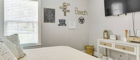 A bedroom with a bed, a television, a wall with motivational signs, and a bedside table with a lamp and a framed picture.