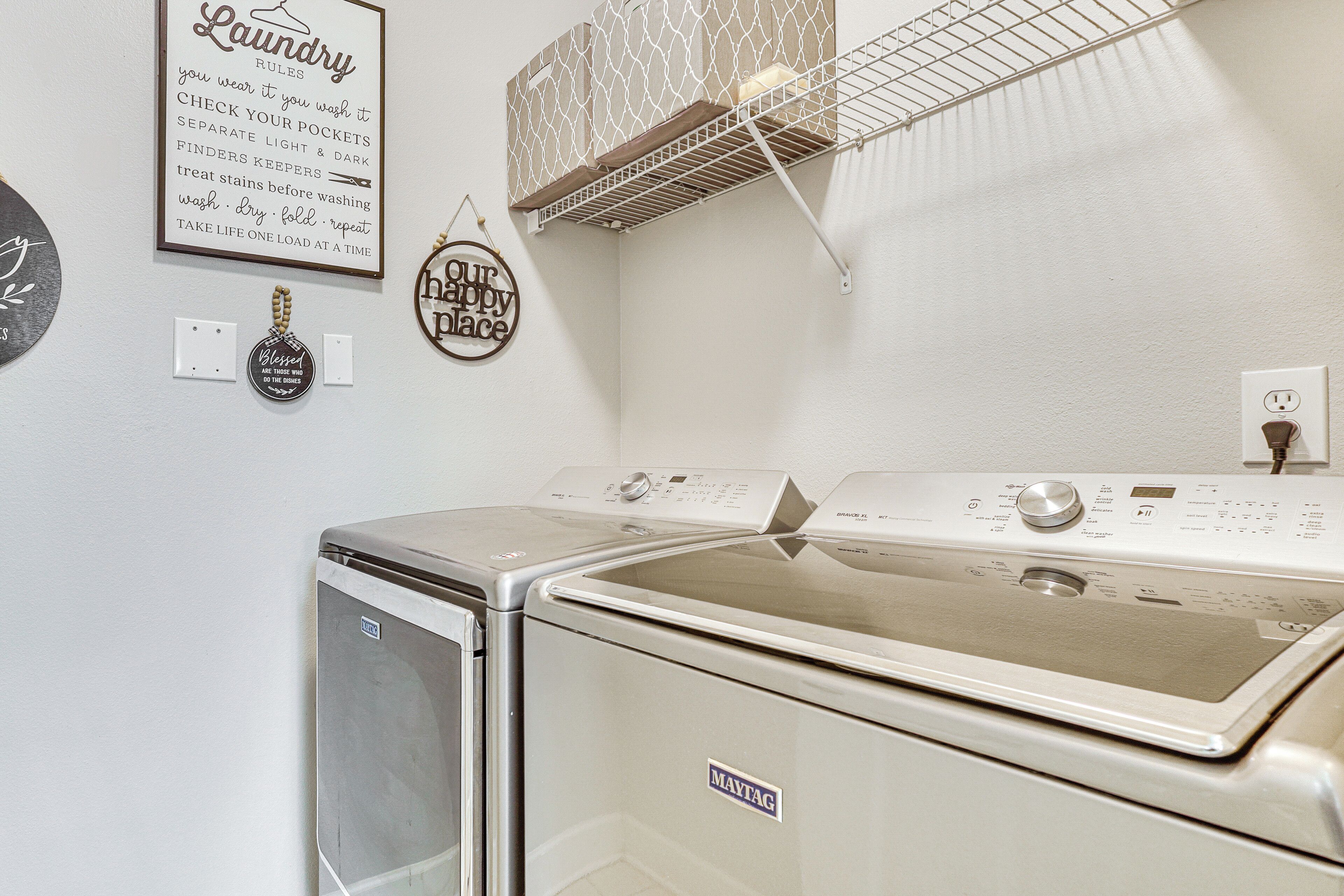 A laundry area with a front-loading washer and dryer, a drying rack, and a wall-mounted light fixture.