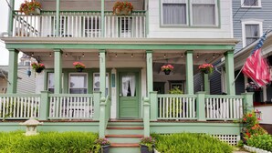 Ein zweistöckiges grünes Haus mit Veranda, weißen Geländern und Blumentöpfen.