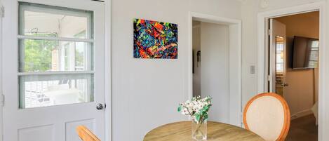 Un coin repas avec une table ronde en bois, deux chaises, un vase de fleurs et une peinture abstraite aux couleurs vives accrochée au mur.