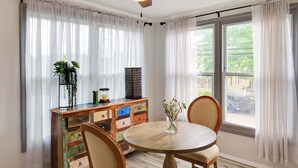 Ein Essbereich mit einem runden Holztisch, zwei Stühlen, einem Deckenventilator und Blick nach draußen durch große Fenster.