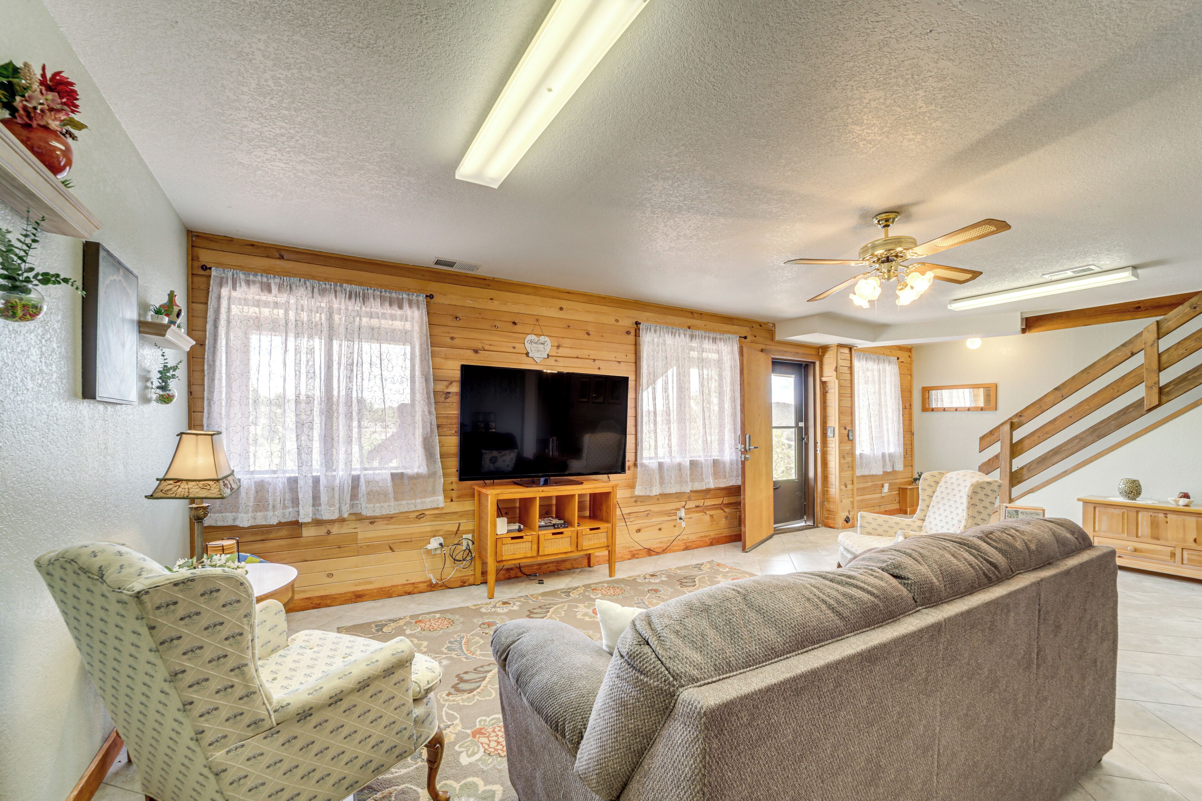 A living room with a television, wooden walls, a ceiling fan, and a staircase.