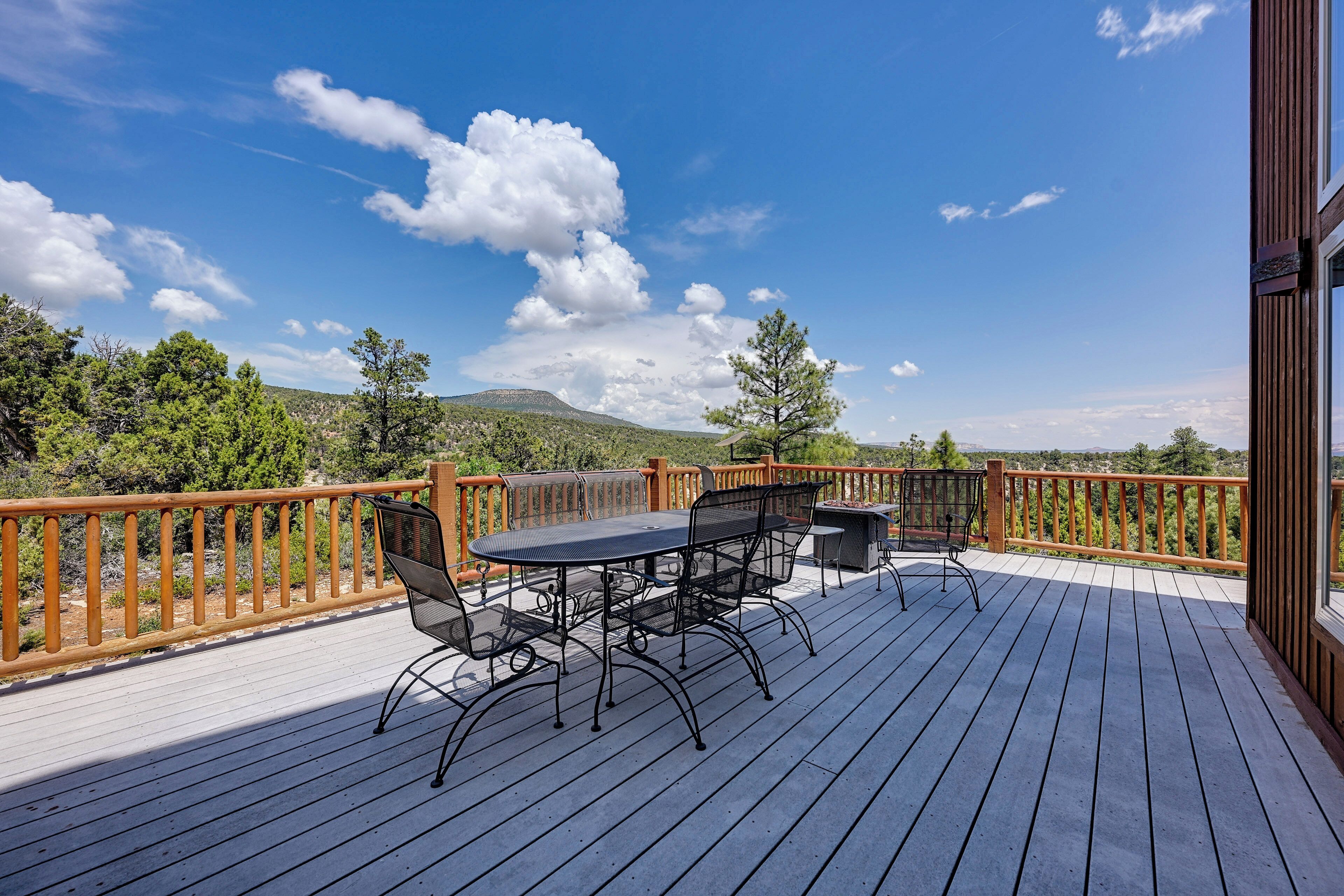 A wooden deck with a table and chairs, overlooking a mountainous landscape.