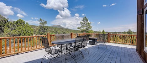 A wooden deck with a table and chairs, overlooking a mountainous landscape.