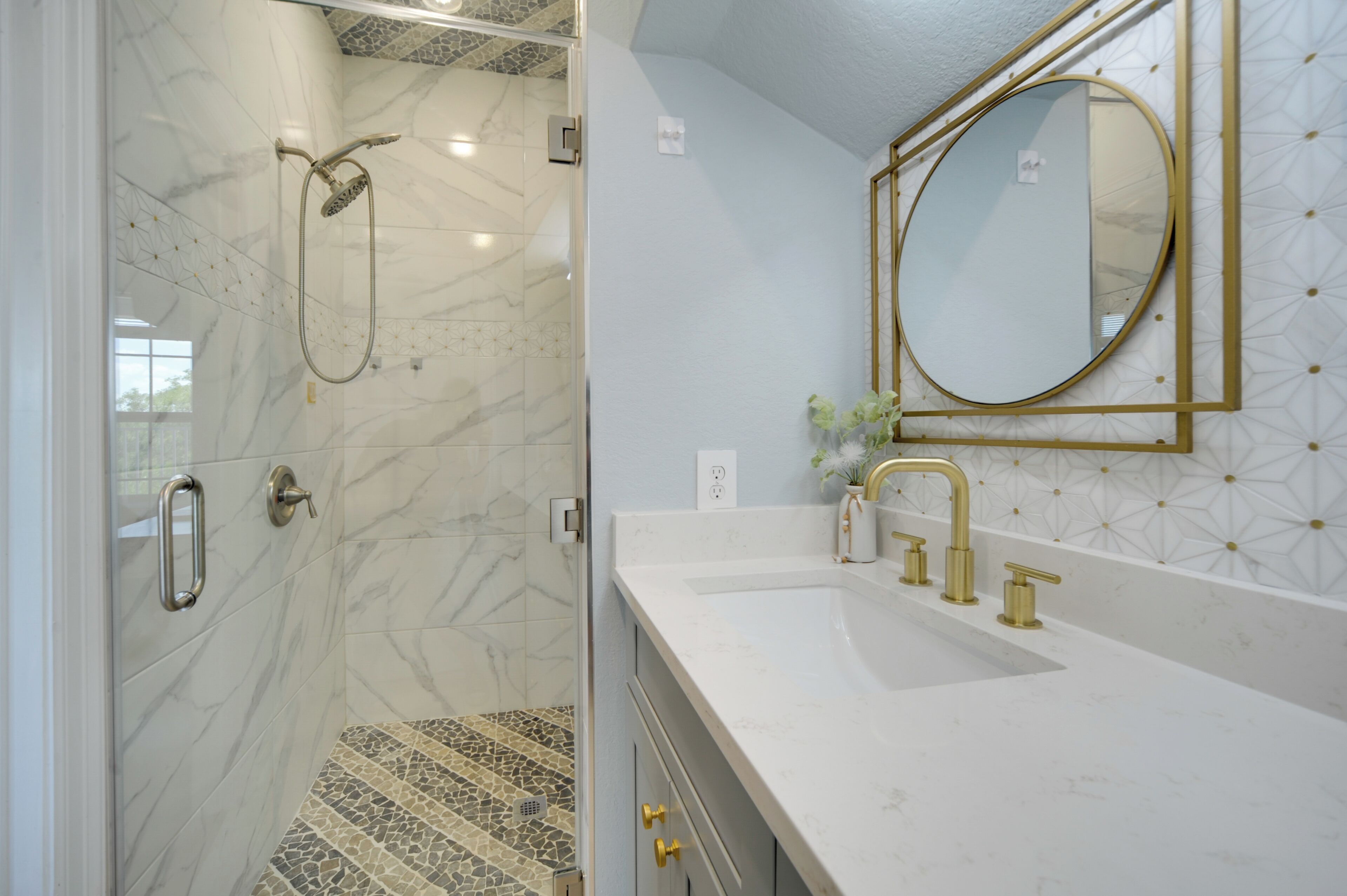 Ein Badezimmer mit Dusche, einem Waschbecken mit goldfarbenen Armaturen und einem Spiegel mit goldener Rahmung.