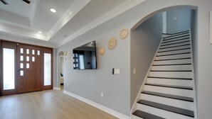 Ein geräumiger Korridor mit Holzboden, einer Treppe mit schwarzen Stufen und einem an der Wand montierten Fernseher.