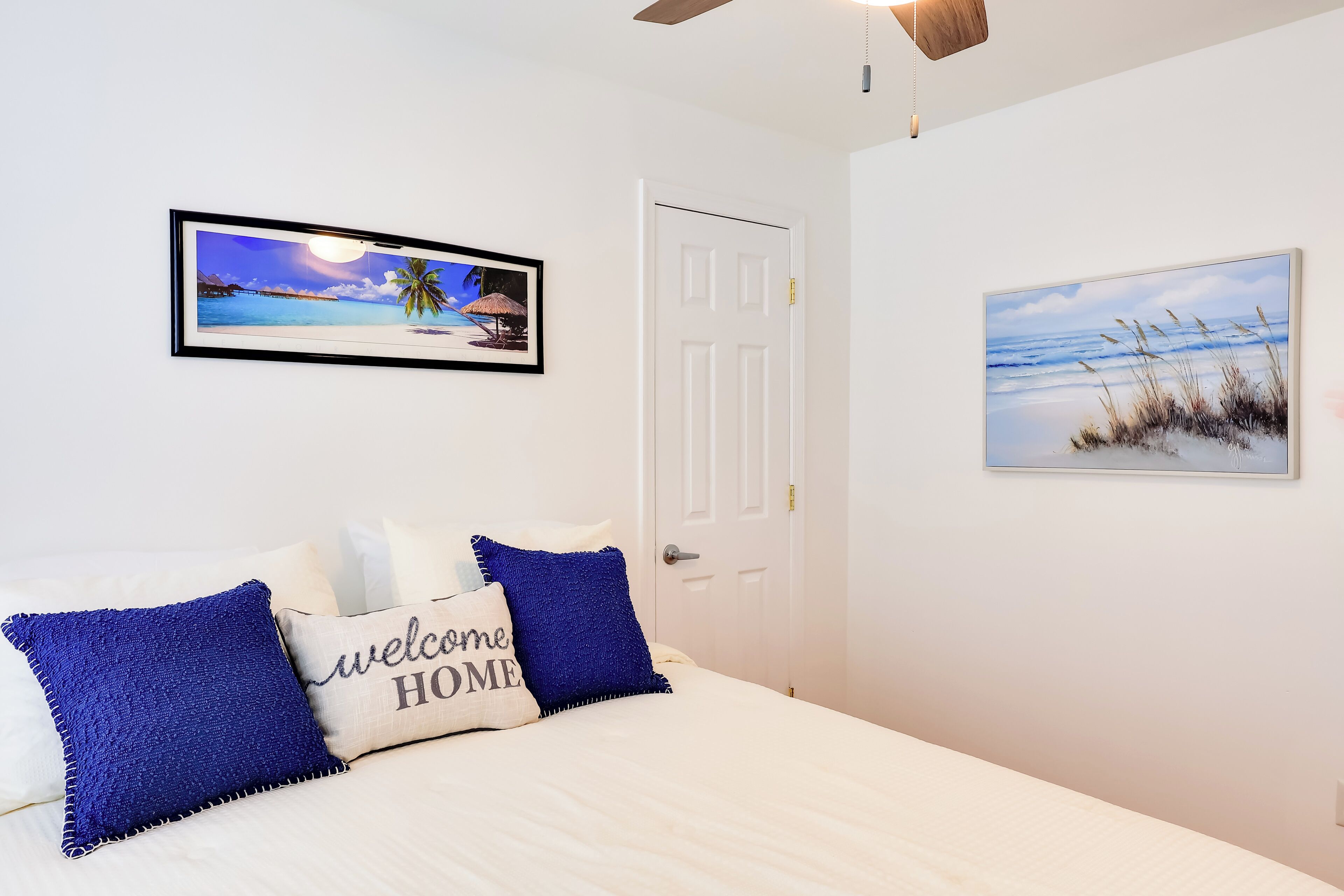Une chambre à coucher avec un lit, deux oreillers, un tableau représentant une plage et une porte.