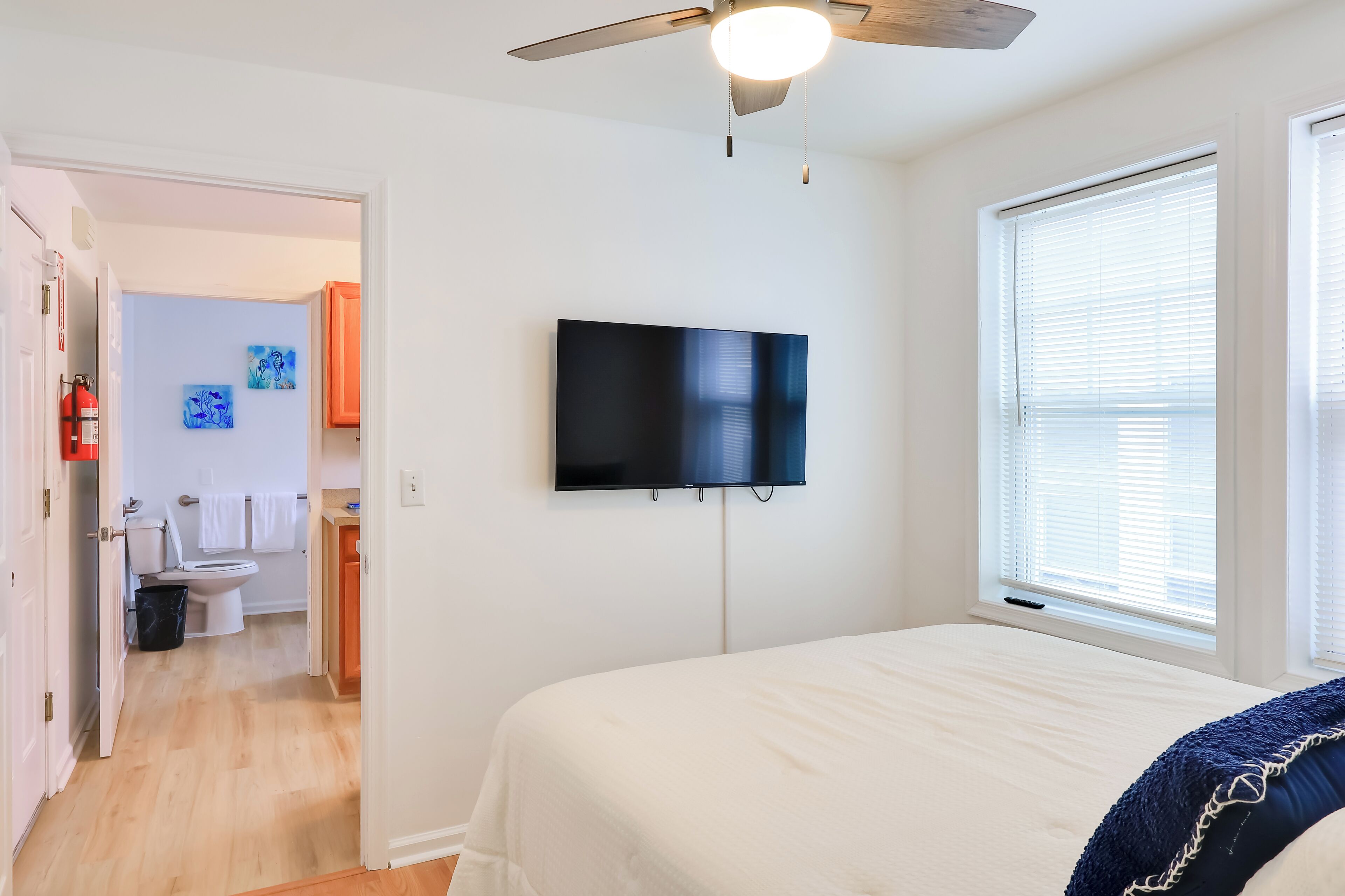 A bedroom with a bed, a ceiling fan, a TV mounted on the wall, and a window with blinds.