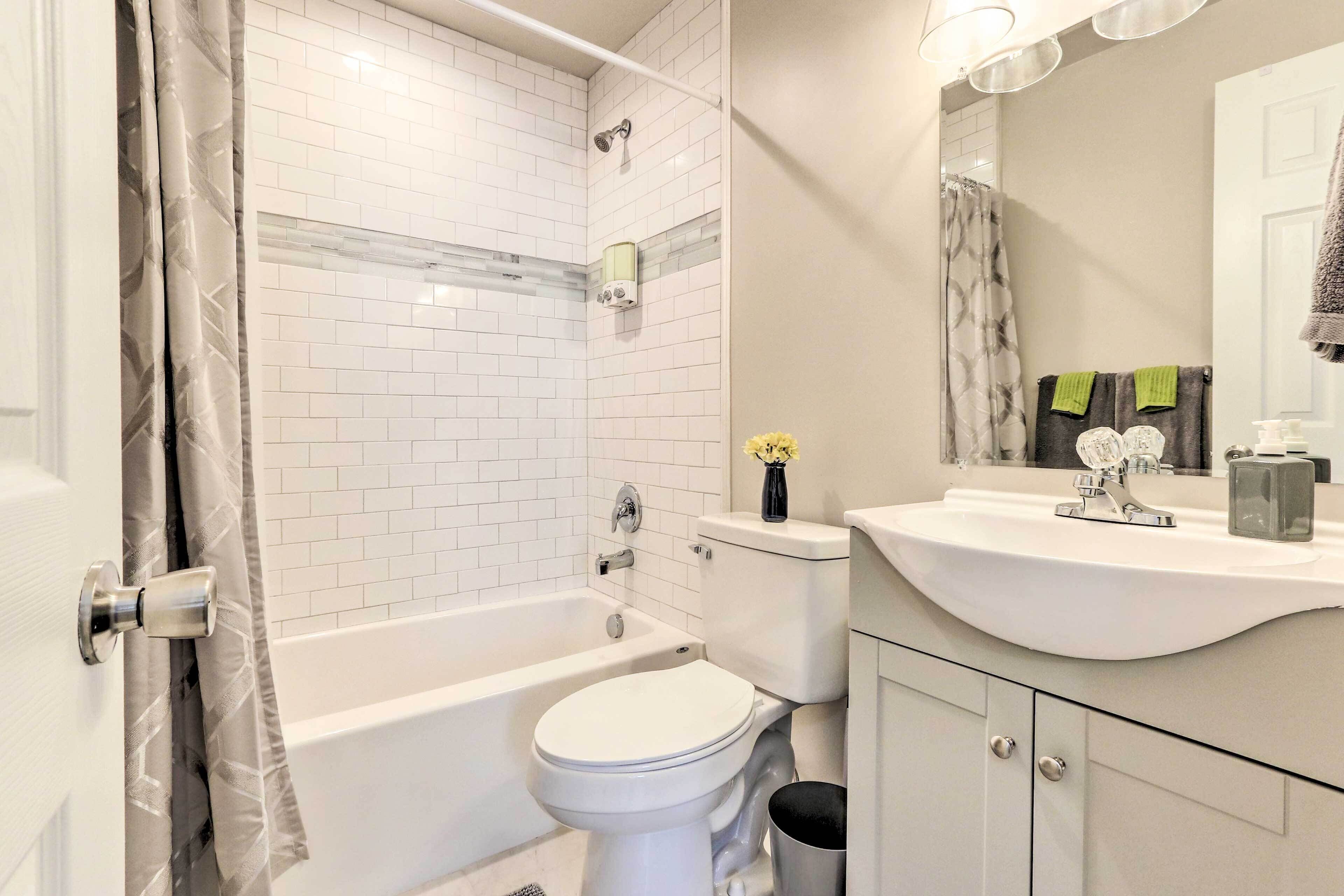 A modern bathroom with a white tiled shower, a bathtub, a toilet, and a sink with a mirror above it.