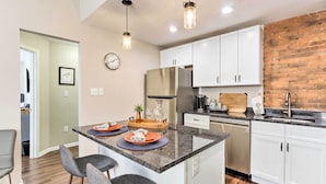 A modern kitchen with white cabinets, a stainless steel refrigerator, and a brick accent wall. - Central Front Royal Getaway on Main Street! (Front Royal)