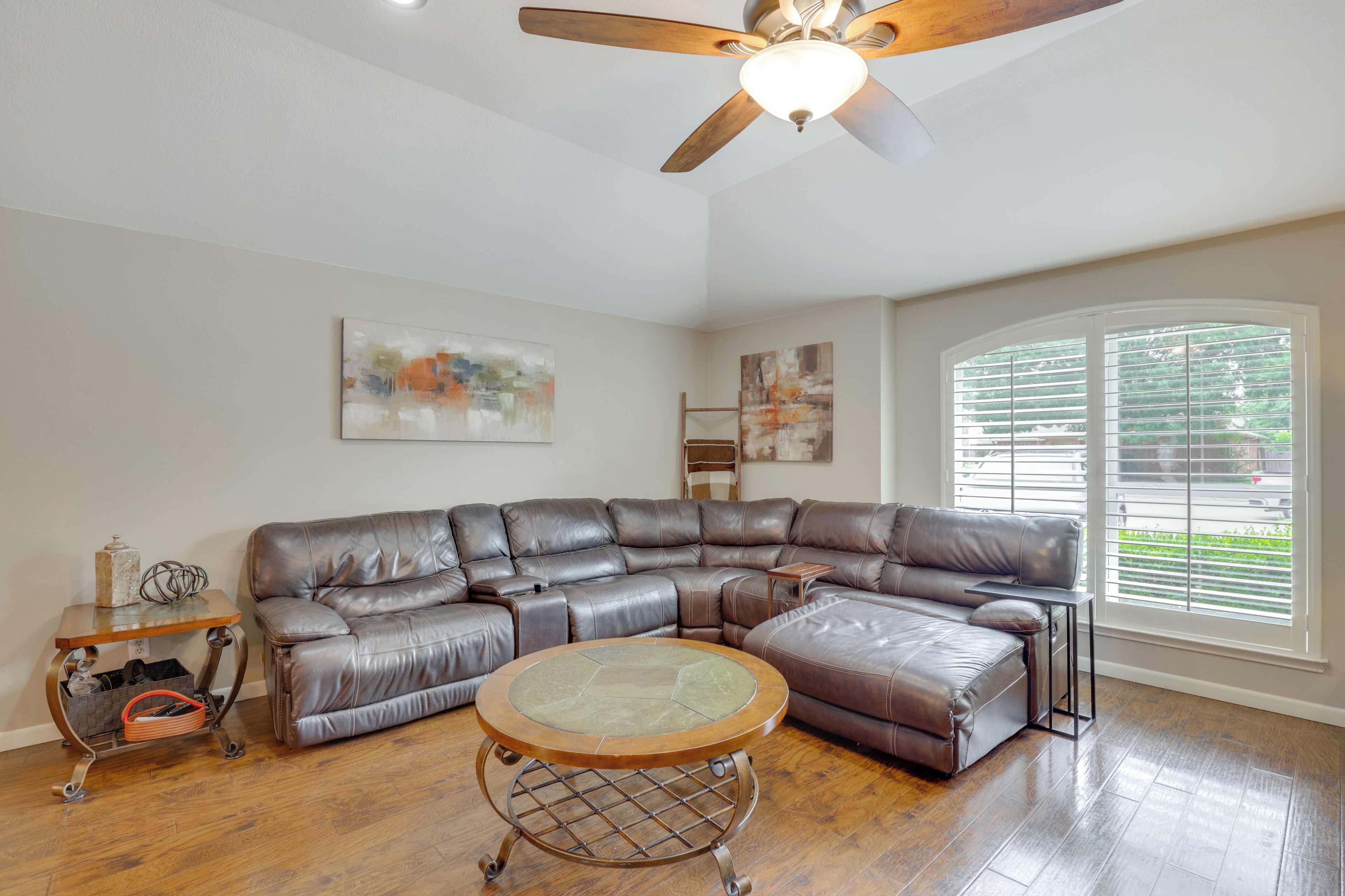 A spacious living room with a large L-shaped sectional sofa, a round coffee table, and a ceiling fan.