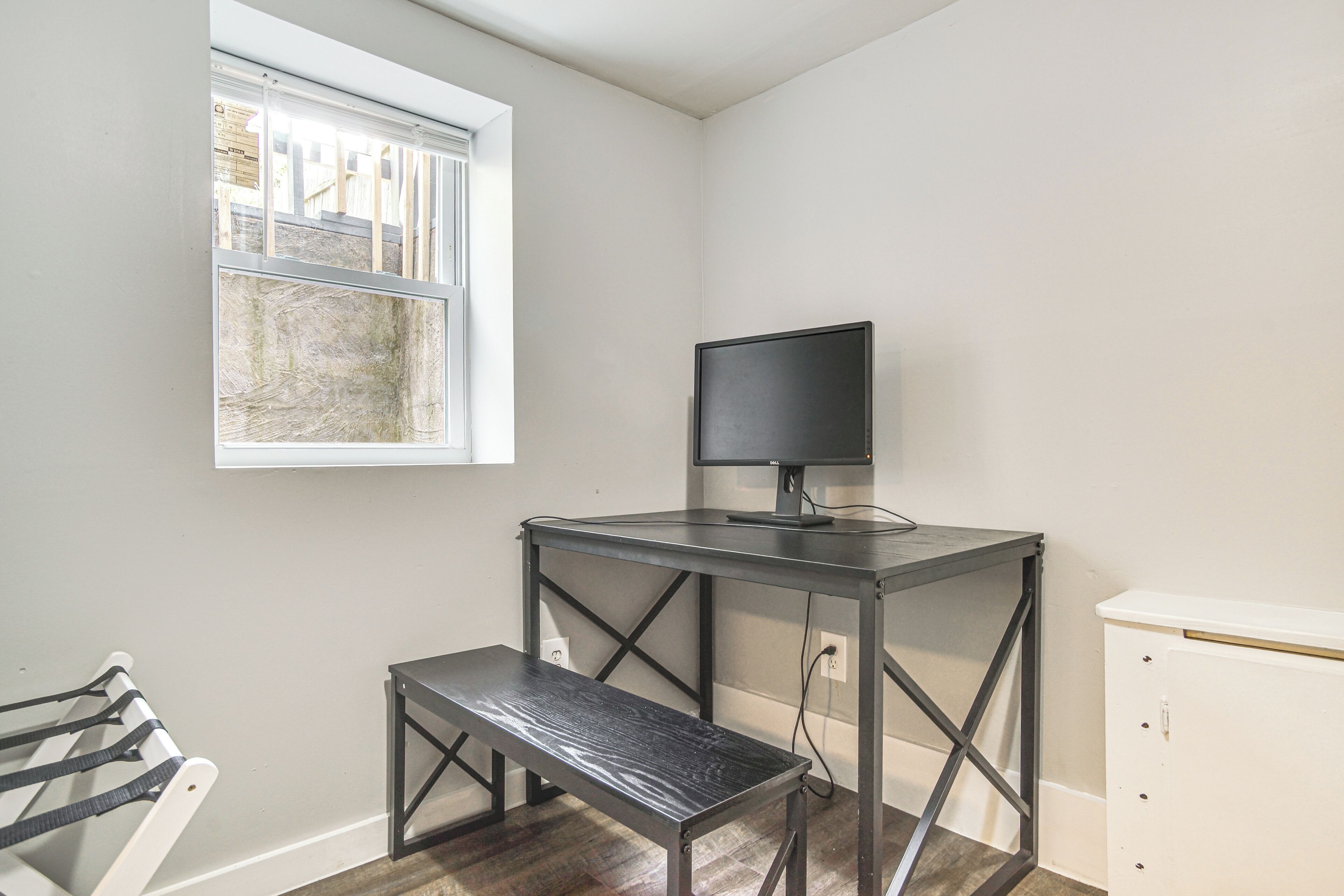 Una habitación pequeña con un escritorio, un banco, una ventana y un armario blanco.