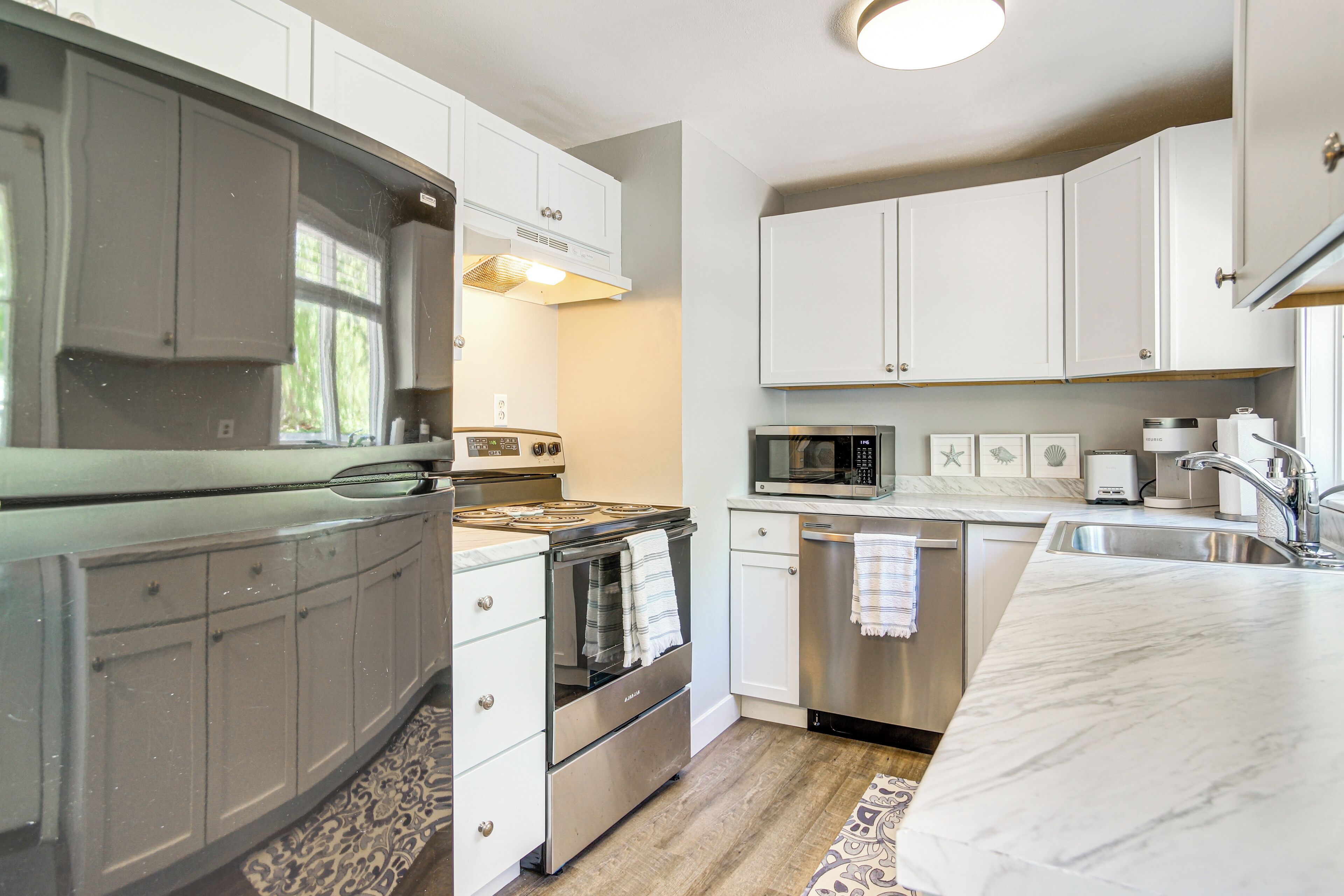 A modern kitchen with white cabinets, stainless steel appliances, and a marble countertop.