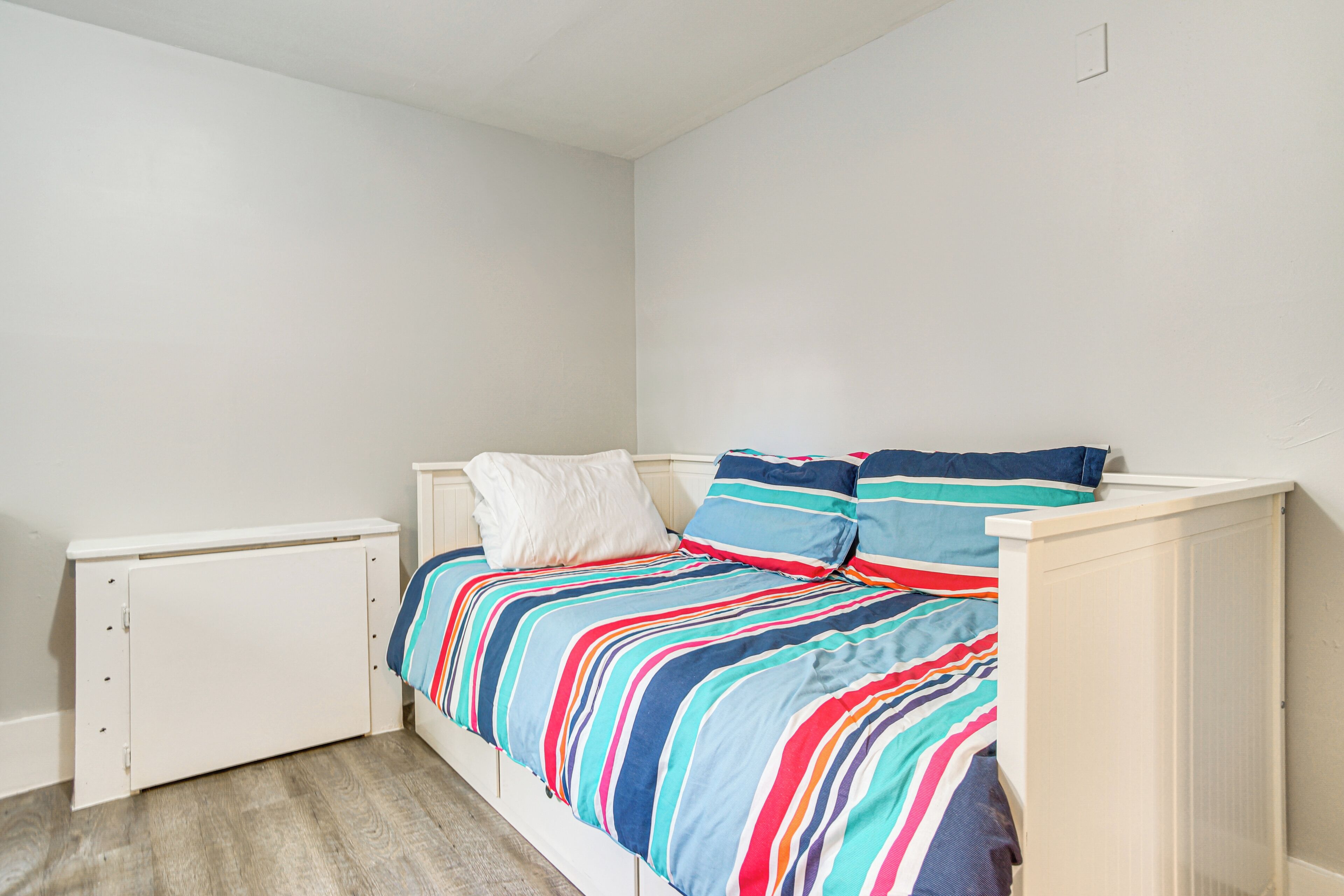 Un dormitorio con cama, paredes blancas y suelo de madera.