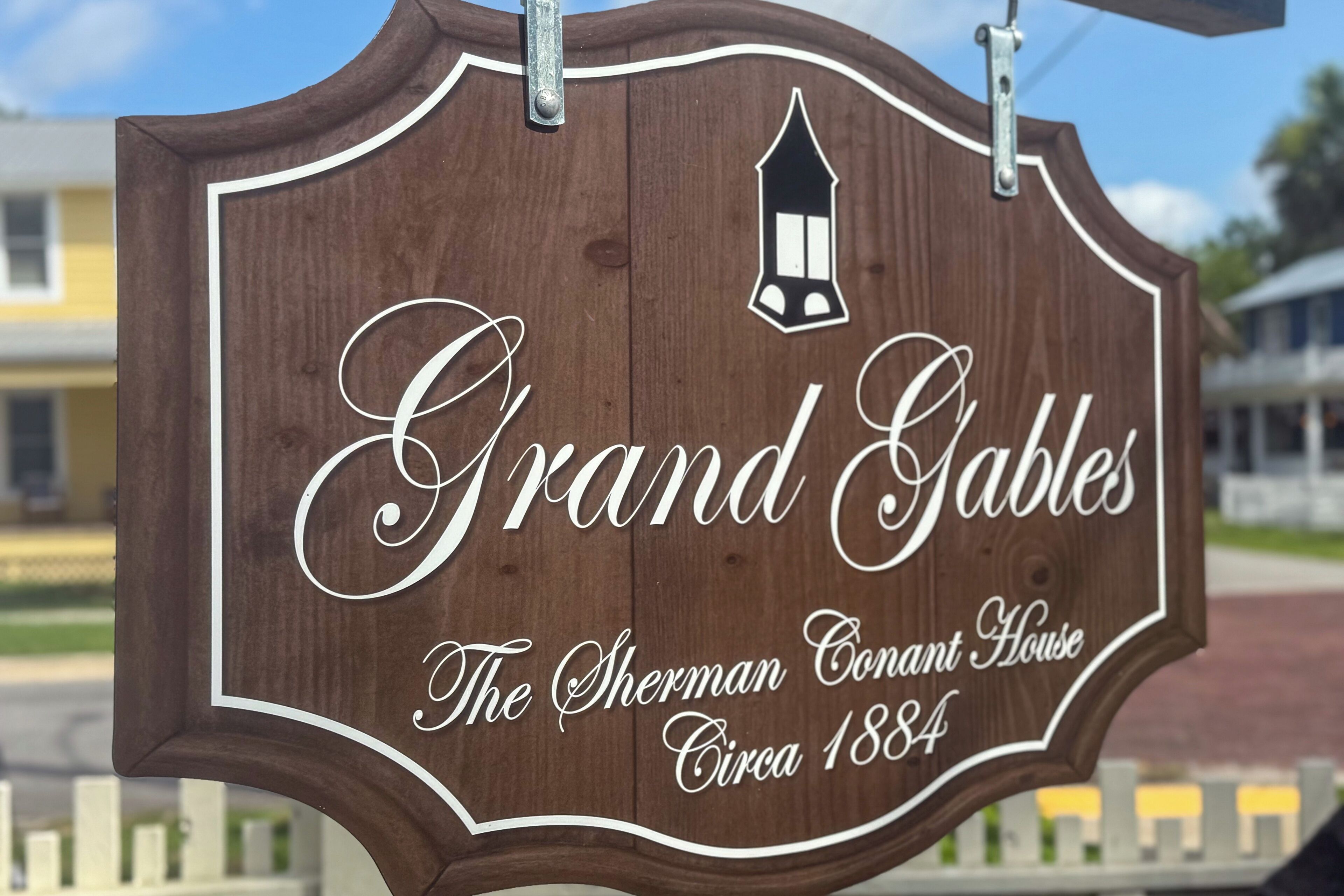 Ein hölzernes Schild mit dem Text "Grand Gables The Sherman Conant House Circa 1884" und einem Laternen-Symbol.
